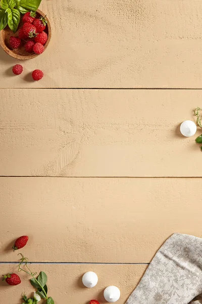 Berries on wooden table top view. Raspberries and mint leaves in wooden bowl, crumpled tablecloth, scattered strawberries and greenery twigs. Rustic style serving, wooden boards decoration