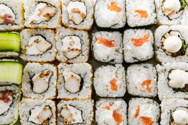 Beyaz arkaplan üst görünümüne ayarlayın. Lezzetli suşi, Asya mutfağı, sağlıklı beslenme, yakın çekim. Geleneksel Japon yemeği, pilav ve salatalık süslemeli balık yemeği, restoran yemeği.