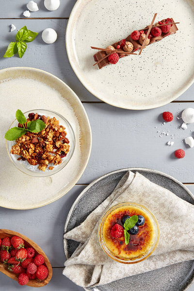 Сладкая еда, десерты в керамических тарелках вид сверху. Fleur de lys молочный шоколад с малиновым конфетом, чиа-пудинг с тайским манго и карамельной гранолой, крем-брюле. Сладкое на деревянном столе
