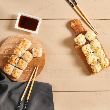 Ahşap tahtaların üstünde fırınlanmış peynir ruloları. Lezzetli sıcak suşi, soya soslu sashimi. Asya yemekleri, geleneksel Japon yemekleri, restoran yemekleri, çubuklu deniz ürünleri.