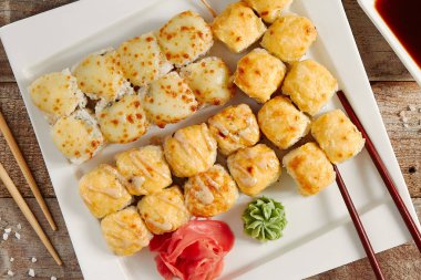 Beyaz tepsi manzaralı fırında rulo. Lezzetli sıcak suşi, wasabi, zencefil ve soya soslu sashimi. Asya yemekleri, geleneksel Japon yemekleri, yemek çubuklarıyla restoran yemekleri.