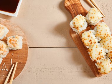 Ahşap tahtaların üstünde fırınlanmış peynir ruloları. Lezzetli sıcak suşi, soya soslu sashimi. Asya yemekleri, geleneksel Japon yemekleri, restoran yemekleri, çubuklu deniz ürünleri.