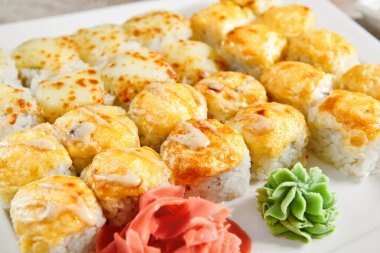 Beyaz tepsi manzaralı fırında rulo. Lezzetli sıcak suşi, wasabi, zencefil ve soya soslu sashimi. Asya yemekleri, geleneksel Japon yemekleri, yemek çubuklarıyla restoran yemekleri.