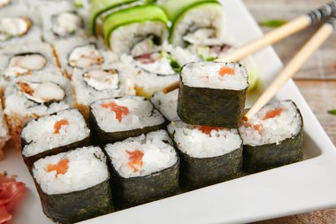 Seramik beyaz tabakta yemek çubuklarıyla yuvarlan. Lezzetli suşi, Asya mutfağı, sağlıklı beslenme, pirinç ve balıklı geleneksel Japon yemekleri. Deniz ürünleri, restoran yemekleri.