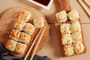 Ahşap tahtaların üstünde fırınlanmış peynir ruloları. Lezzetli sıcak suşi, soya soslu sashimi. Asya yemekleri, geleneksel Japon yemekleri, restoran yemekleri, çubuklu deniz ürünleri.