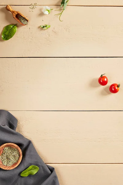 Flavoring and napkin on wooden table top view. Crumpled tablecloth, spices in wooden bowl and bucket, flower buds, greenery and tomatoes on wooden boards. Rustic style decoration, table setting