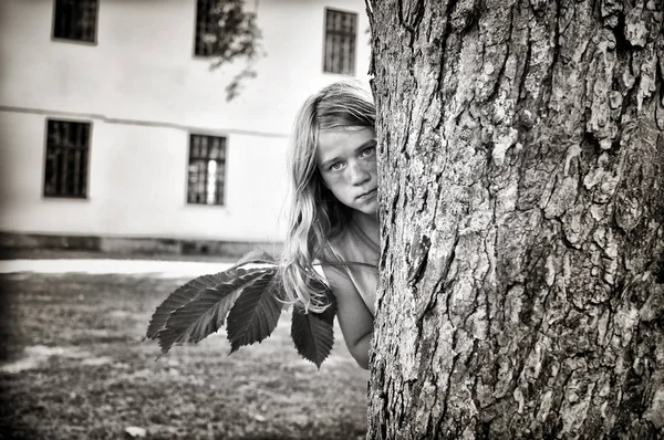 Fille se faufilant derrière un arbre — Photo