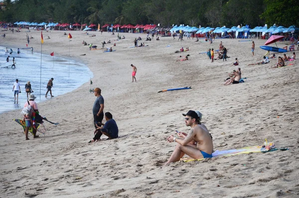 Místní obyvatelé a toustovači na přeplněné pláži Kuta na Bali populární tra — Stock fotografie