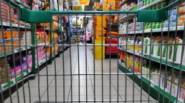 Süpermarketteki rafların arasında bir alışveriş arabası var.