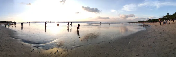 Люди наслаждаются впечатляющим закатом на пляже в Куте, Бали — стоковое фото