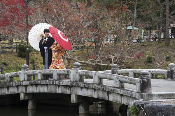 Young couple in colorful kimonos walking on a stone bridge in Ma