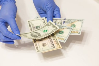 Tıbbi eldiven takan eller beyaz arka planda dolar banknotları sayıyor