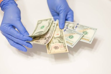 Tıbbi eldiven takan eller beyaz arka planda dolar banknotları sayıyor