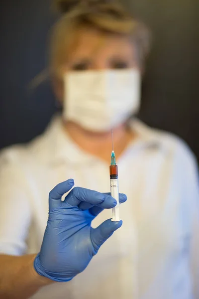 Senior woman wearing mask, gloves holds a syringe in hand. Selective focus. Coronavirus and epidemic virus symptoms.