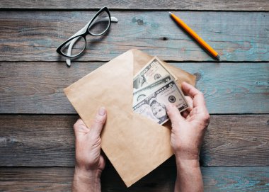 Kadınların ellerini kapayarak Amerikan dolarlarını ahşap masanın üzerindeki bir zarfa koyuyorlar.