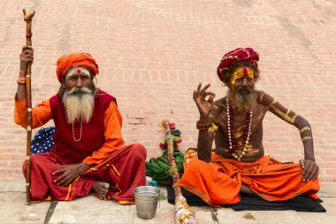 Varanasi, Hindistan - 3 Ocak 2020: Kimliği belirlenemeyen iki Hindu sadhu kutsal adamı, Hindistan 'ın Varanasi kentindeki Ganj nehrinin kenarında oturuyor. Turizm, Varanasi 'ye pek çok sahte sadhus çekti.
