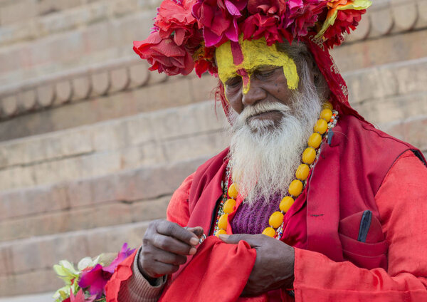 VARANASI, INDIA - JANUARY 03, 2020 : Unidentified Hindu sadhu holy man, sits on the ghat near the Ganges river in Varanasi, India.  