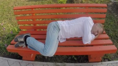 Kot pantolon ve tişört açık havada bir bankta uyuyan adam