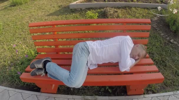 Uomo in jeans e camicia che dorme su una panchina sotto il cielo aperto — Video Stock