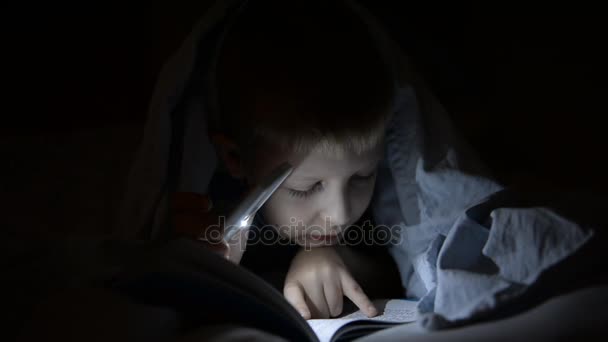 A boy with a flashlight under a blanket is reading a book. Shkolnik, emotions, secrets, horrors, laughter — Stock Video