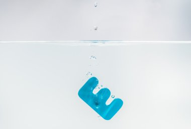 Mavi ahşap alfabe E beyaz arka plan ve seçici odak ile su damla