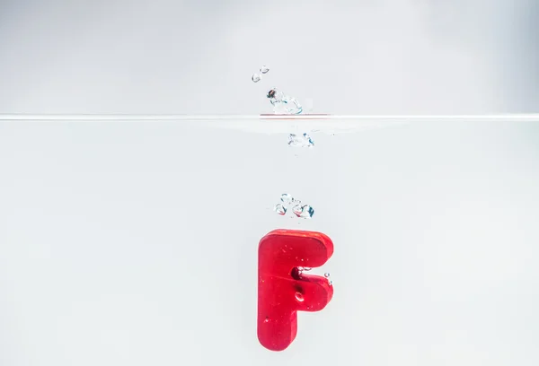 Alfabeto de madeira vermelho F gota na água com fundo branco e foco seletivo — Fotografia de Stock