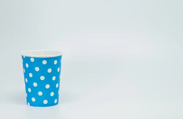 Белый точечный рисунок на синей бумажной чашке с белым фоном и выборочным фокусом — стоковое фото