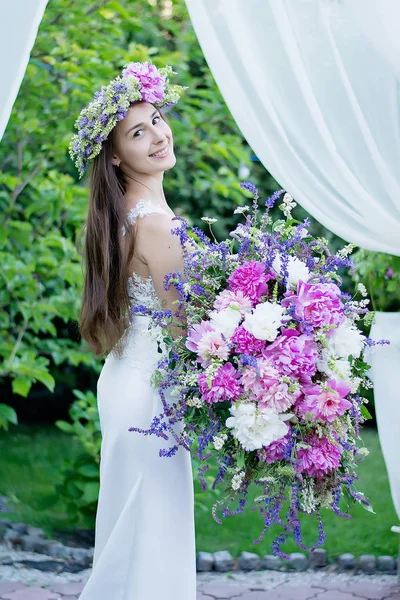 Happy bride with flowers and in a wreath outdoors