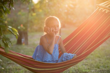 Hamakta dinlenen genç bir kadın. Genç bir kadın parkta kitap okuyor.