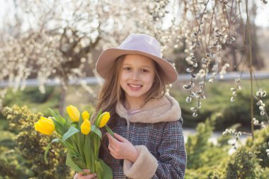 Bahar parkında sarı lale demeti olan şapkalı küçük bir kız.