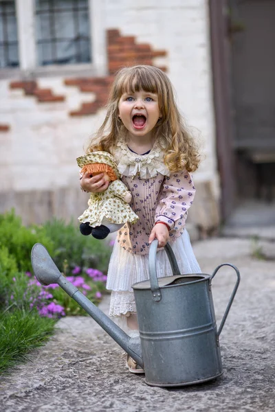 庭に水やり缶と人形を持った女の子がいて — ストック写真