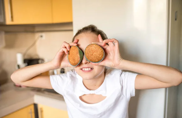 girl holding cupcakes covering eyes. Preteen girl having fun in kitchen