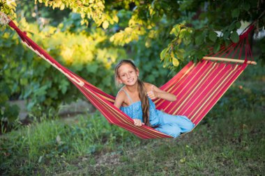 Hamakta dinlenen genç bir kadın. Parkta kitap okuyan genç bir kadın. Kız telefonda selfie çekiyor ve hamakta dinleniyor..