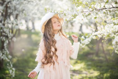 Bahar bahçesinde pembe elbise ve retro şapka giyen küçük kız.