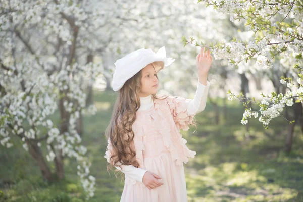 春の庭でピンクのドレスとレトロな帽子をかぶった女の子 — ストック写真