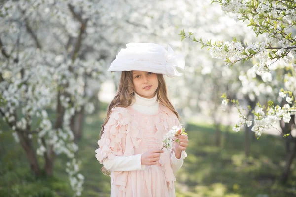 在春天的花园里 小女孩穿着粉红色的衣服 头戴一顶复古的帽子 — 图库照片