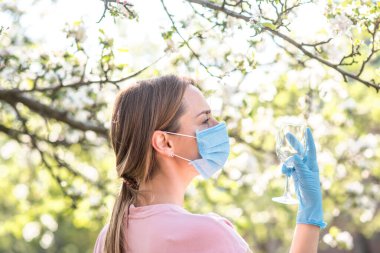 Coronavirus. Yüzü maskeli kadın karantinada. Evde kal. Evde yemek pişirmenin tadını çıkar. Aile kavramı. Genç bir kadın karahindiba üflüyor. Sahilde bir bardak şampanya. Suyla oynayan kadın. Kadın şişeden su içiyor.