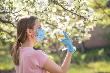 Coronavirus. Yüzü maskeli kadın karantinada. Evde kal. Evde yemek pişirmenin tadını çıkar. Aile kavramı. Genç bir kadın karahindiba üflüyor. Sahilde bir bardak şampanya. Suyla oynayan kadın. Kadın şişeden su içiyor.