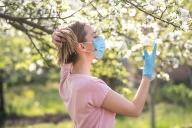 Coronavirus. Yüzü maskeli kadın karantinada. Evde kal. Evde yemek pişirmenin tadını çıkar. Aile kavramı. Genç bir kadın karahindiba üflüyor. Sahilde bir bardak şampanya. Suyla oynayan kadın. Kadın şişeden su içiyor.