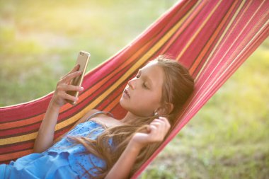 Güzel bir kız hamakta dinleniyor. Kız telefonda selfie çekiyor. Aile memnuniyeti. Bir yaz günü dinlenin. gülümseyen çocuk.