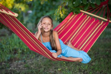 Güzel bir kız hamakta dinleniyor. Kız telefonda selfie çekiyor. Aile memnuniyeti. Bir yaz günü dinlenin. gülümseyen çocuk.