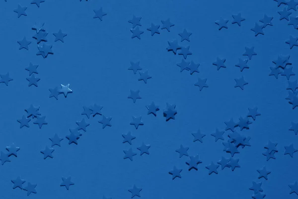 Lentejuelas azules sobre un fondo azul brillante con confeti como asteriscos . —  Fotos de Stock