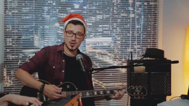 산타 모자를 쓴 재능있는 청년 이 홈 스튜디오에서 새로운 곡을 녹음 하고 있습니다. — 비디오