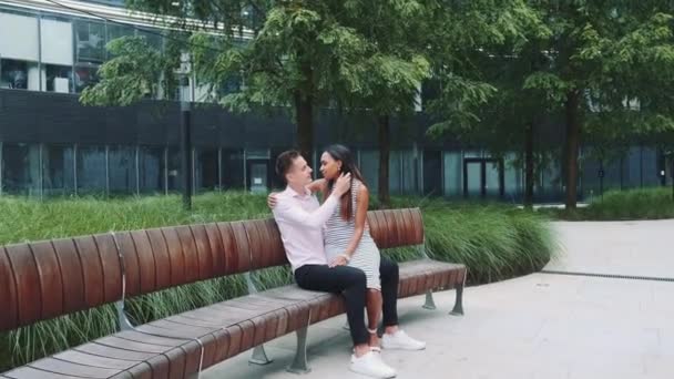 Zoom plan de jeune couple multiethnique assis sur le banc et s'embrassant — Video