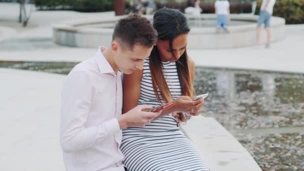 Multiethnic couple sitting together outdoors and looking in the smartphones — 图库视频影像