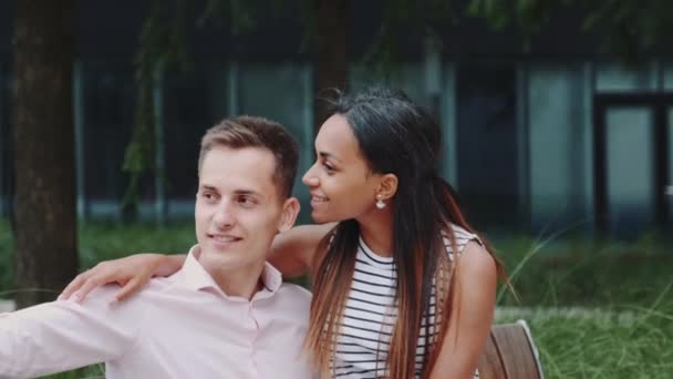 Couple romantique multiethnique assis sur un banc dans le parc et prenant selfie — Video