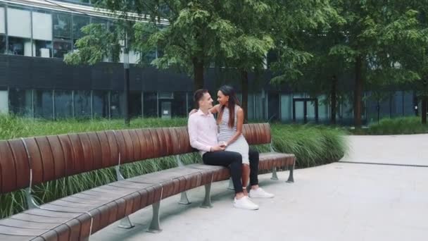 Zoom colpo di giovane uomo baciare le sue amiche mano seduta su panchina nel parco — Video Stock
