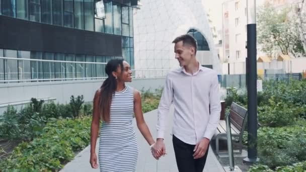 Мультирасовая влюбленная пара, идущая по улице, держащаяся за руки и целующаяся — стоковое видео