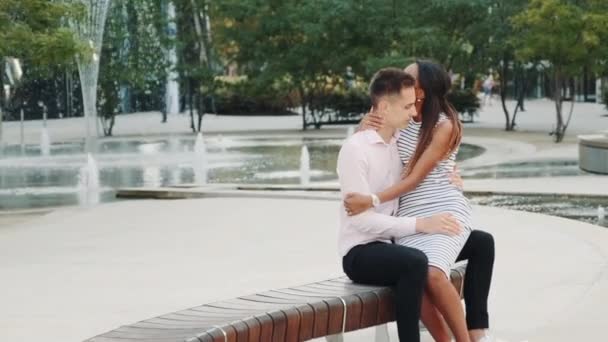Vegyes bőrű férfi és szerelmes nő ülnek a padon a parkban, ölelkeznek és beszélgetnek. — Stock videók