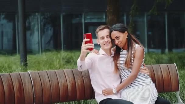 Plan panoramique d'une femme souriante métissée et d'un homme prenant du selfie dans un parc — Video
